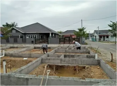 Site work on a RumahHQ house at foundation stage — workers levelling soil between finished concrete ground beams, on a residential street