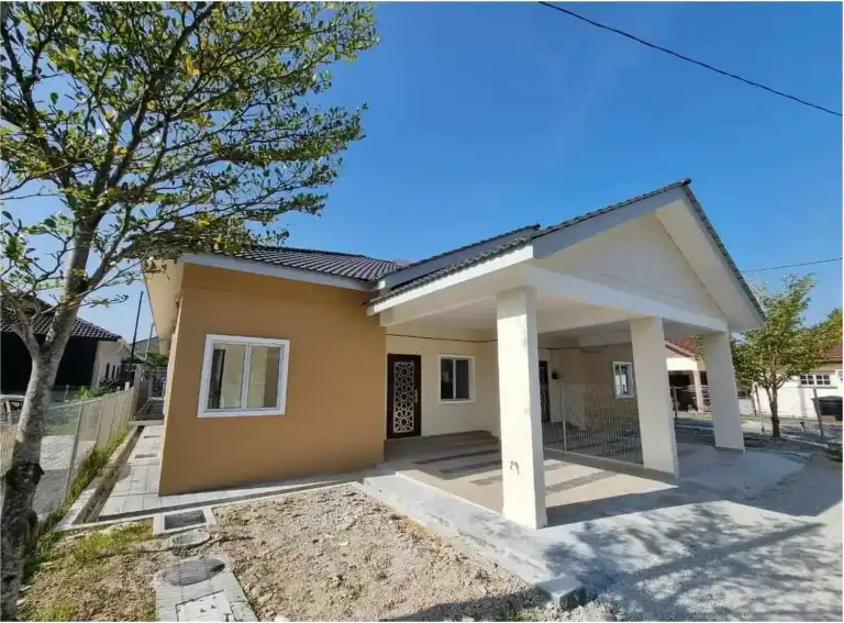 Completed single-storey bungalow built by RumahHQ — mustard and cream external walls, dark roof tiles, a gable-roofed carport on two concrete columns, a geometric wrought grille door, and a gravel yard awaiting landscaping