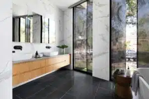 Modern bathroom with large windows, marble walls, double sinks, and sleek black fixtures.