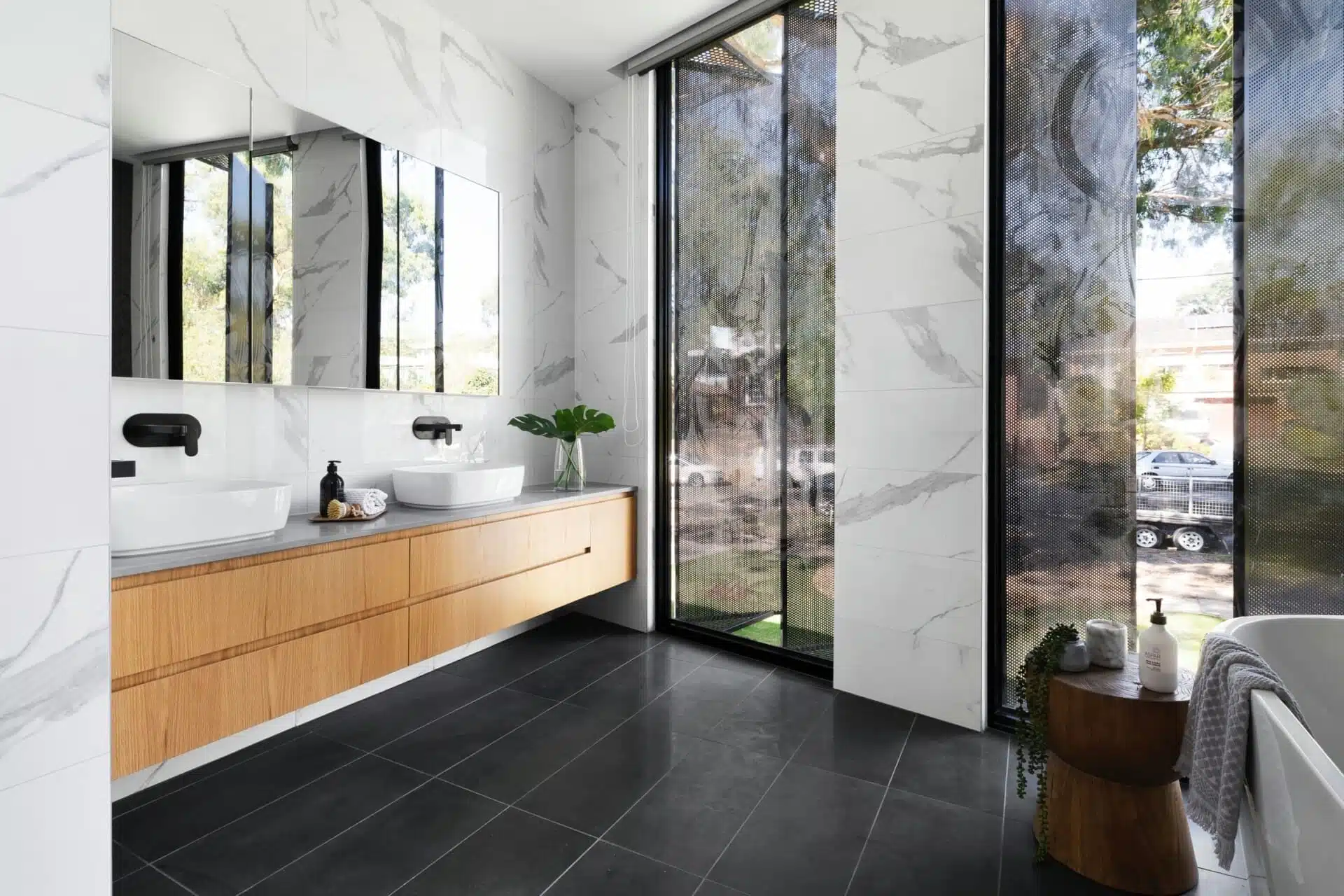 Modern bathroom with large windows, marble walls, double sinks, and sleek black fixtures.