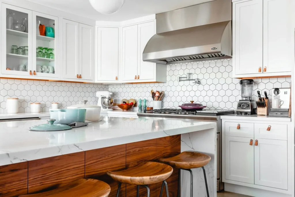 Modern kitchen with white cabinets, hexagon tile backsplash, and marble island with wooden bar stools.