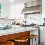Modern kitchen with white cabinets, hexagonal tile backsplash, and wooden stools around a marble island countertop.