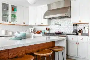 Modern kitchen with white cabinets, hexagonal tile backsplash, and wooden stools around a marble island countertop.