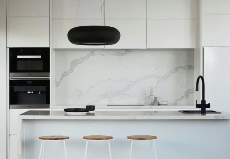 Penjimatan Hebat dengan Harga Wiring Rumah Terbaik! 5 Minimalist white kitchen with marble backsplash, black faucet, modern pendant light, and wooden bar stools.