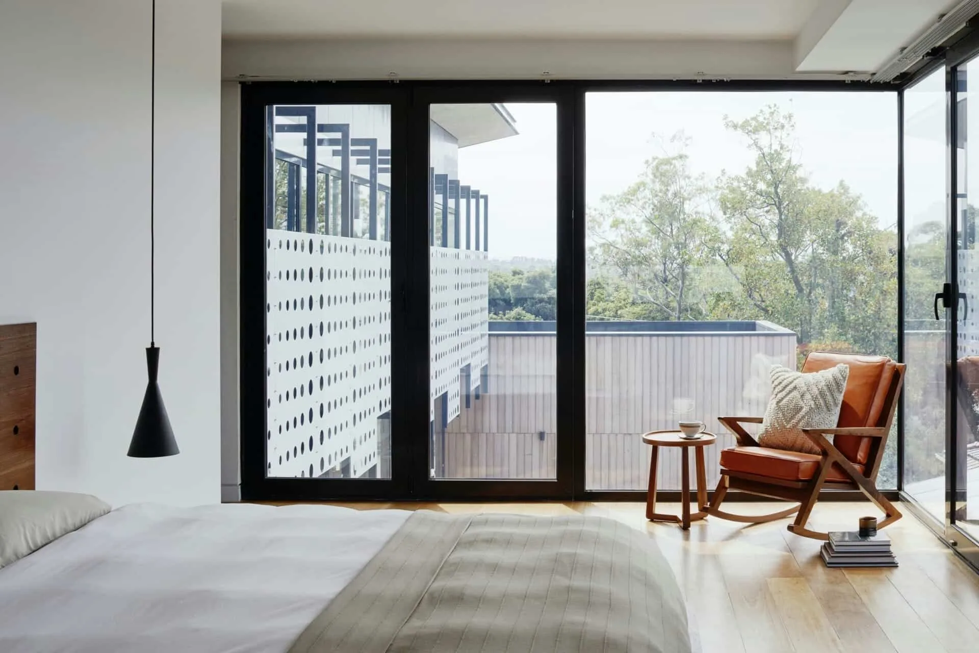 Modern bedroom with large windows, wooden chair, and nature view for tranquil relaxation.