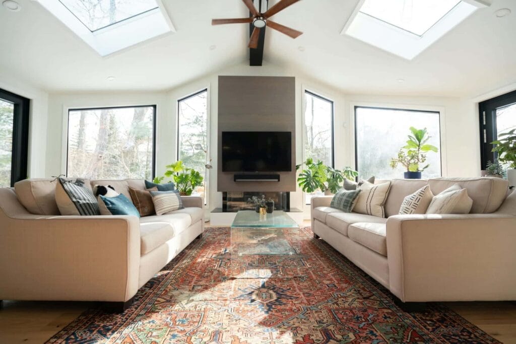 Modern living room with skylights, cozy couches, vibrant rug, and indoor plants for a bright, inviting space.
