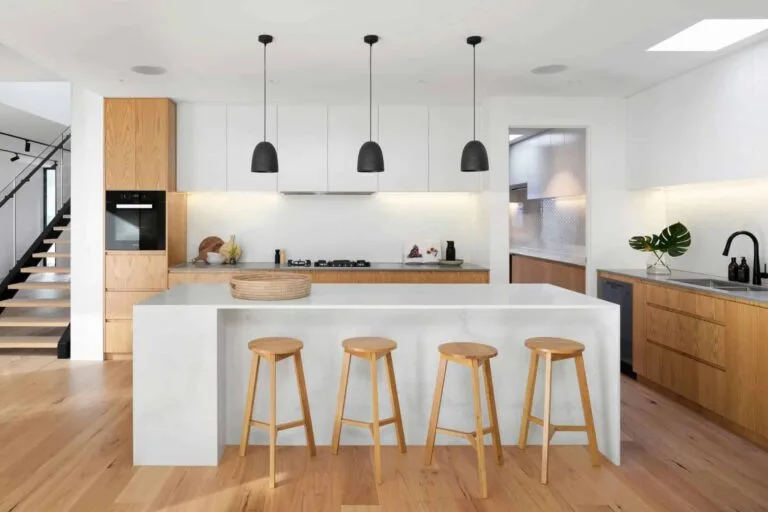 Bina Rumah 800–2,000 sqft: Rahsia Anggaran Kos Yang Kontraktor Tak Nak Anda Tahu 3 Modern kitchen with wooden stools, sleek white island, pendant lights, and wood cabinetry. Minimalist and stylish design.