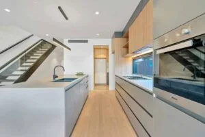Modern kitchen with sleek cabinetry, built-in oven, and contemporary lighting under a staircase.