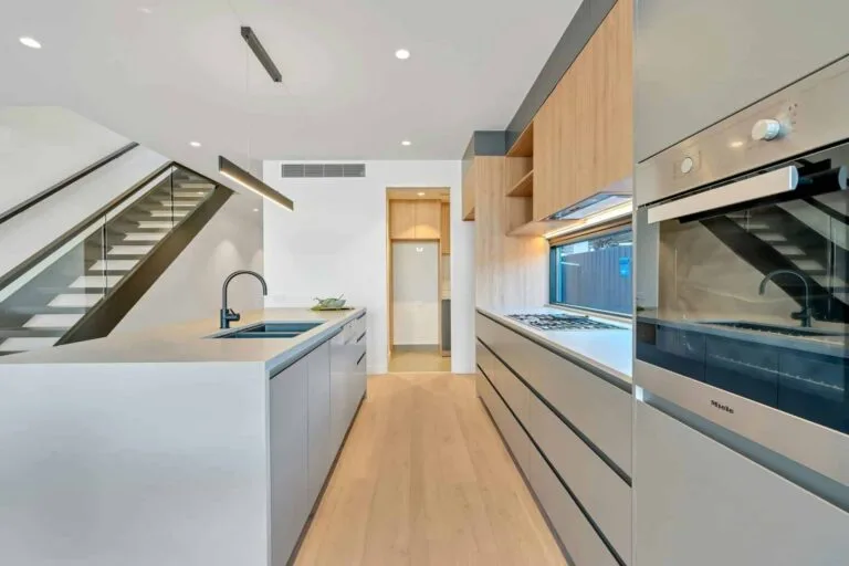Modern kitchen with sleek cabinetry, built-in oven, and contemporary lighting under a staircase.