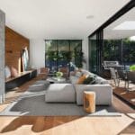 Modern living room with large windows, cozy seating, and outdoor dining area, blending indoor and outdoor spaces.