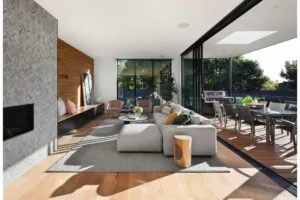 Modern living room with large windows, cozy seating, and outdoor dining area, blending indoor and outdoor spaces.