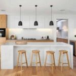 Modern kitchen with wooden cabinets, island with stools, pendant lights, and sleek white countertops.
