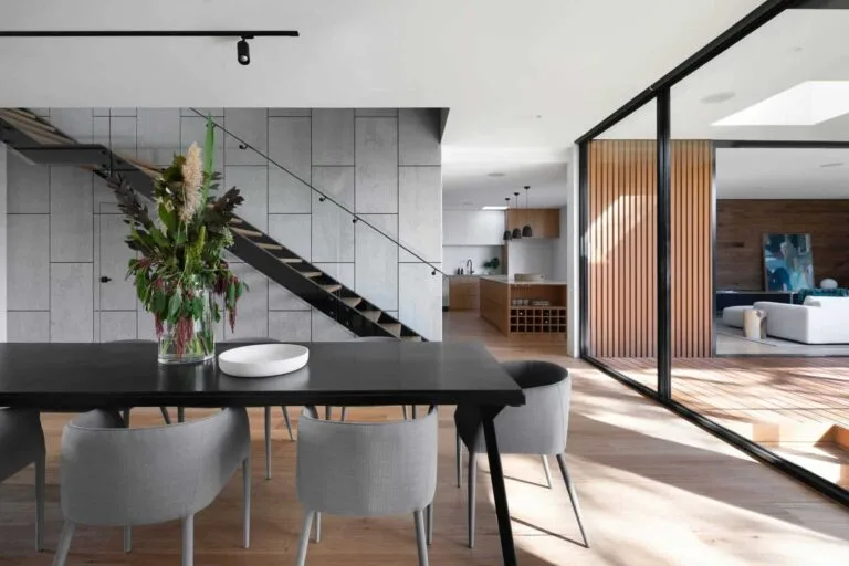 Berapa Tahun Tempoh Pinjaman Rumah Terbaik untuk Anda? 5 Modern open-plan dining room with stylish decor, sleek staircase, and natural light through large glass doors.