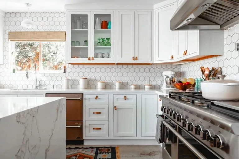 Modern kitchen with white cabinets, hexagonal tiles, stainless steel appliances, and a large countertop.