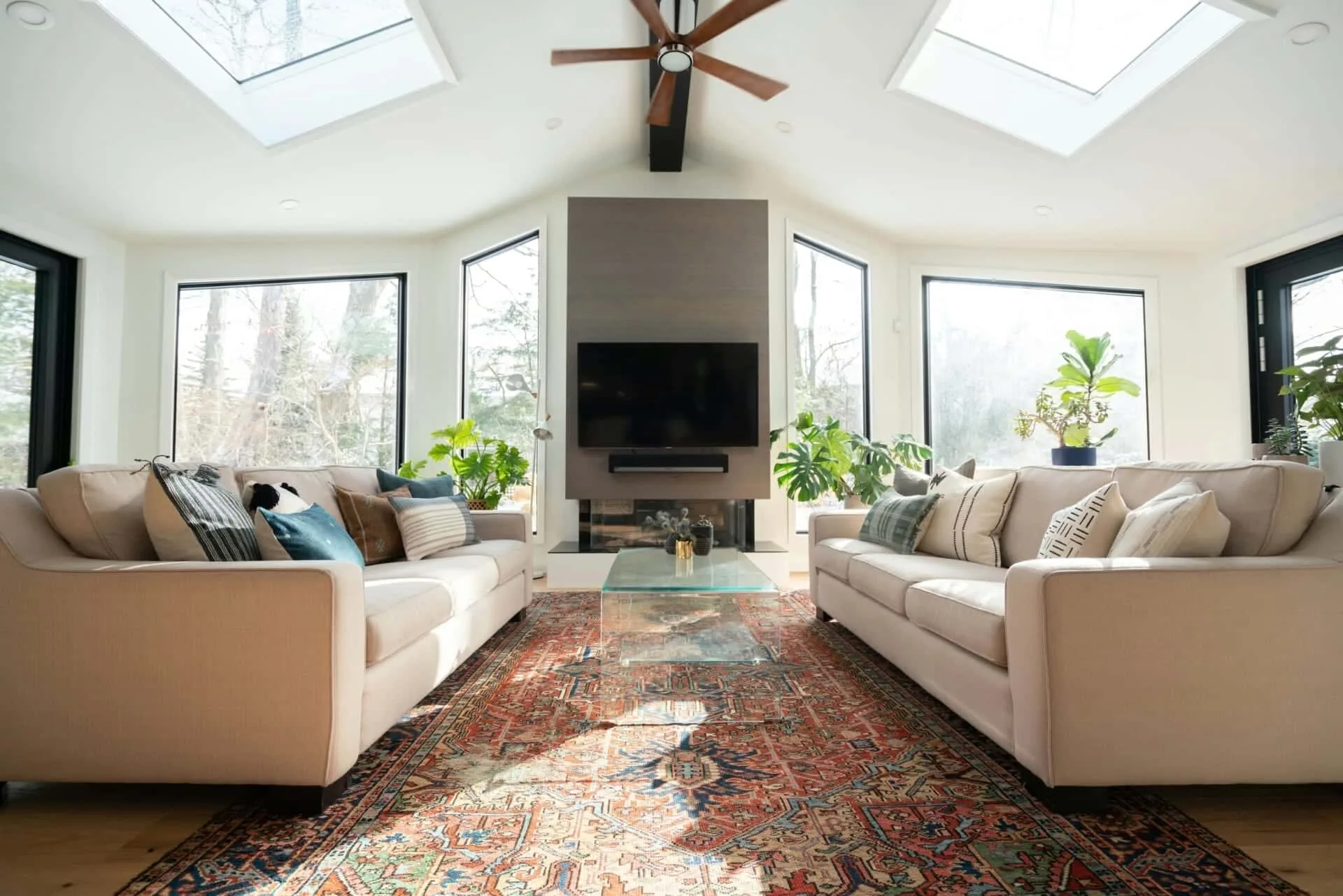 Bright modern living room with skylights, beige sofas, vibrant carpet, and indoor plants. Cozy and elegant decor.