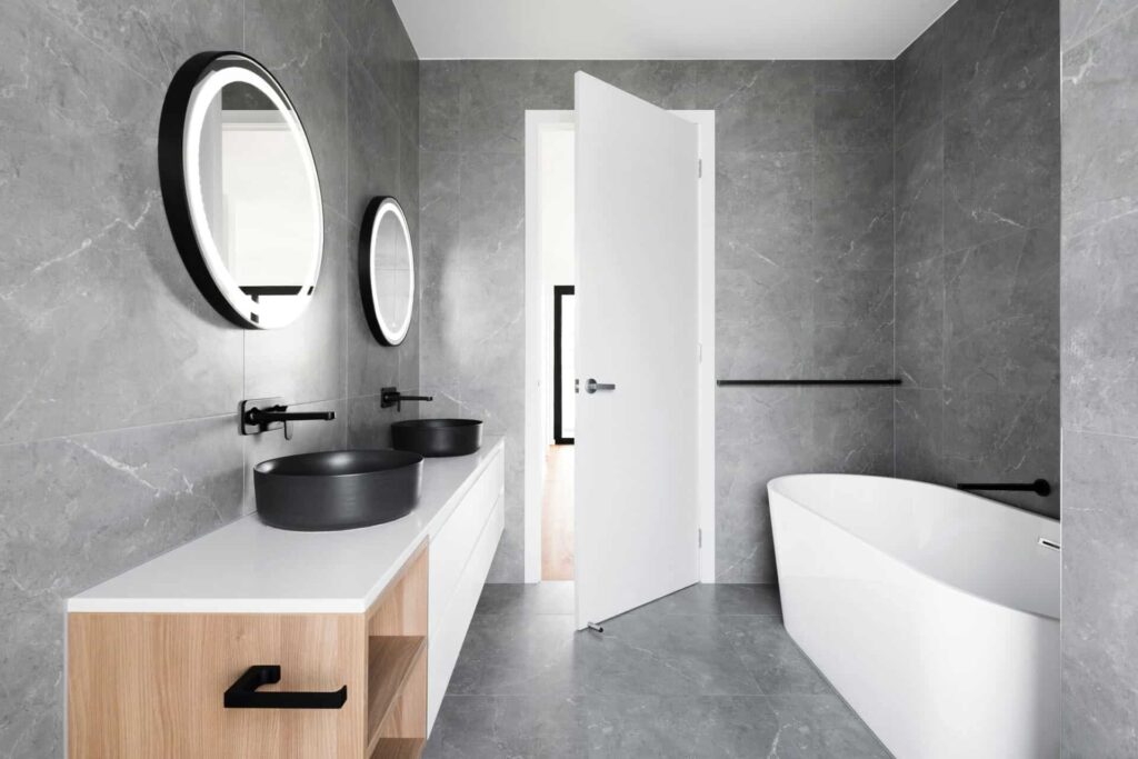 Modern gray bathroom with dual round mirrors, black sinks, and a sleek white bathtub.