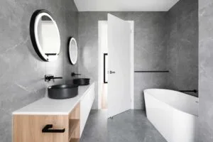 Modern gray bathroom with dual round mirrors, black sinks, and a sleek white bathtub.