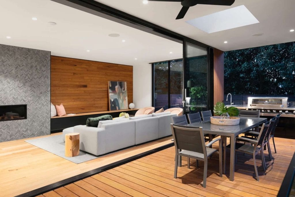 Modern indoor-outdoor living space with a cozy sofa, dining table, and patio, featuring wood accents and a ceiling fan.
