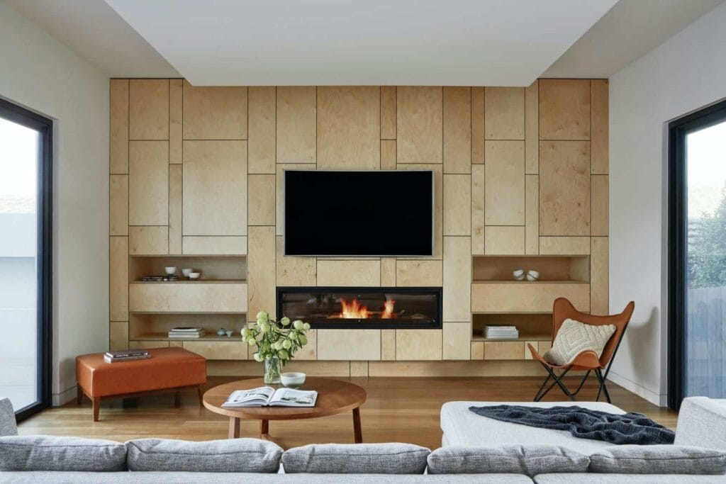 Modern living room with wood paneling, TV, fireplace, cozy furniture, and a coffee table adorned with green foliage.