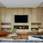 Modern living room with wood paneling, TV, fireplace, cozy furniture, and a coffee table adorned with green foliage.