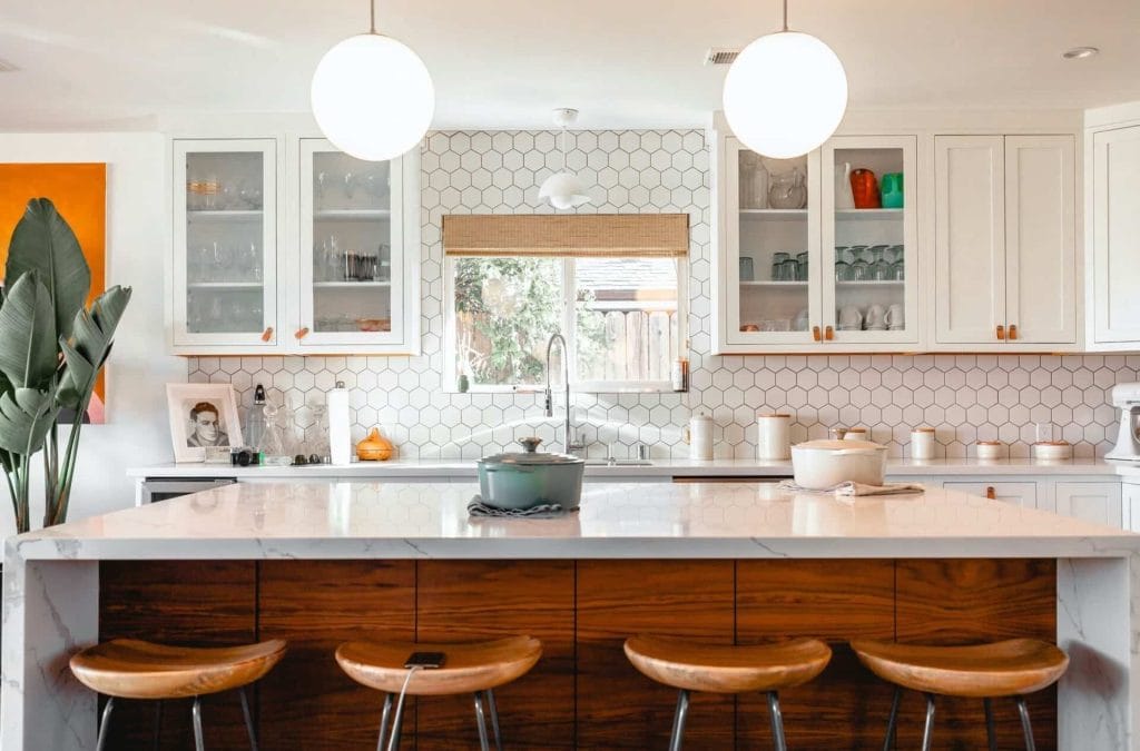 Modern kitchen with hexagon tile backsplash, wooden stools, and pendant lighting over a white marble island countertop.