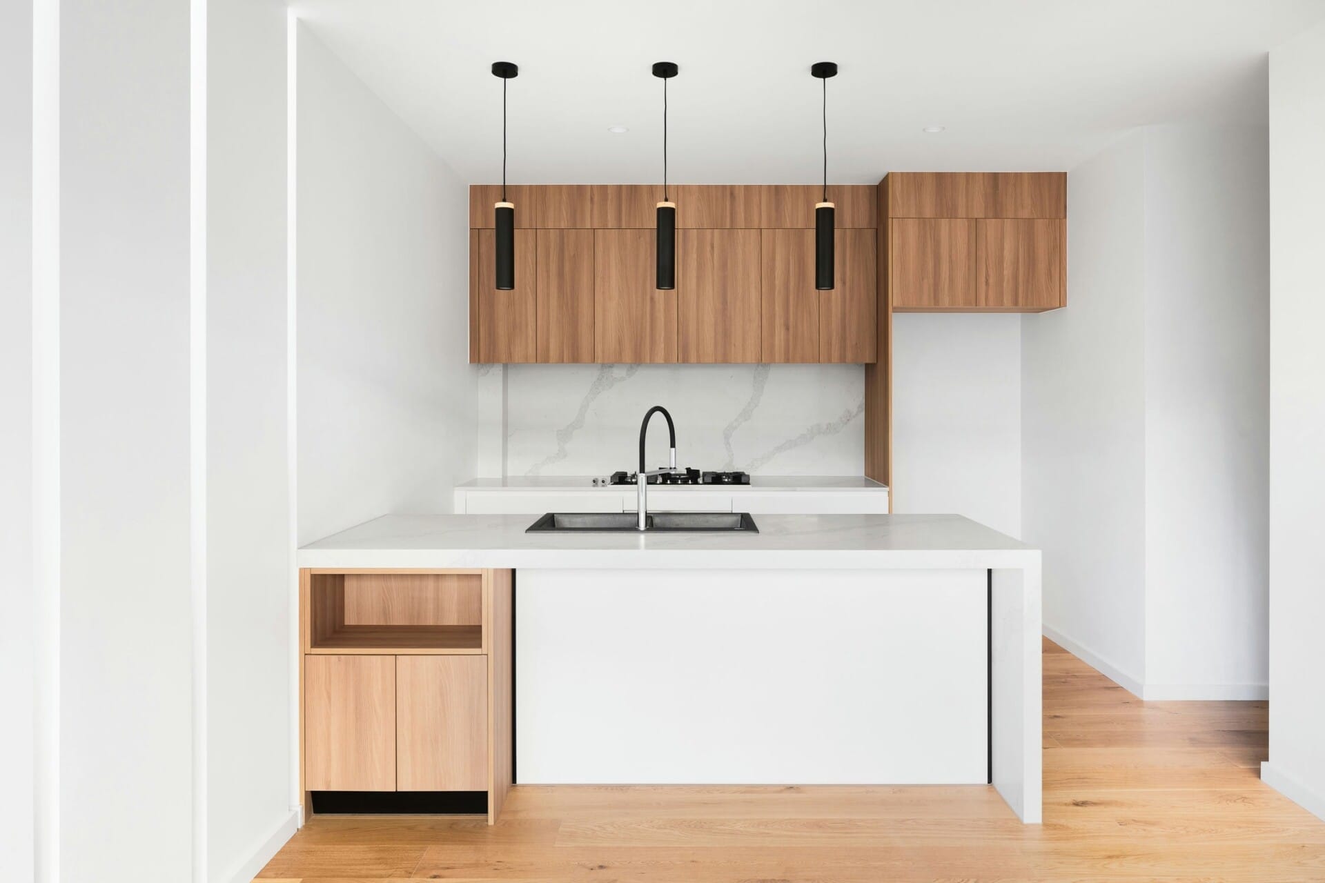 Modern minimalist kitchen with wooden cabinets, marble backsplash, and pendant lights over a white island countertop.