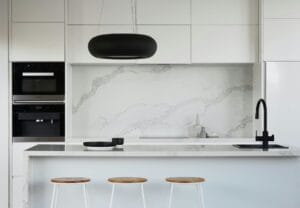 Modern minimalist kitchen with white cabinets, marble backsplash, black faucet, and bar stools.