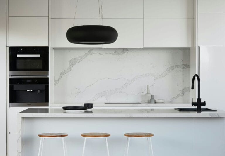 Modern minimalist kitchen with white cabinets, marble backsplash, black faucet, and bar stools.